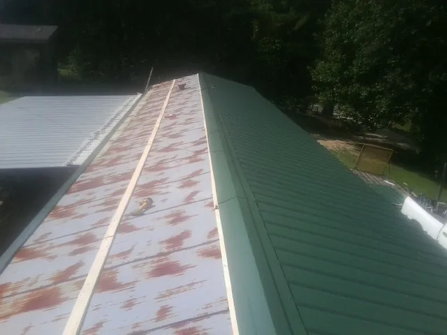 Old rusted panels beside newly installed green metal roofing — Wind Damage Roof Repair by Roofing Brothers in Stoughton