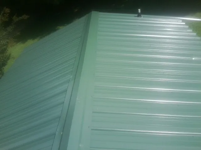 New green metal panels meeting at the ridge of a roof — Flat Roof Repair work by our crew in Stoughton