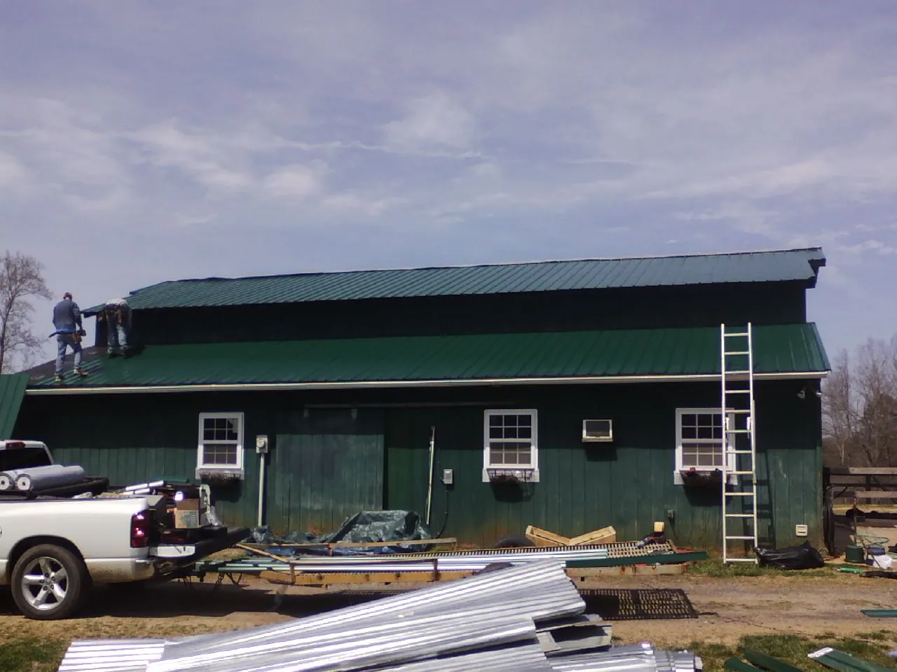 Crew installing green metal roofing on a large green barn in Stoughton