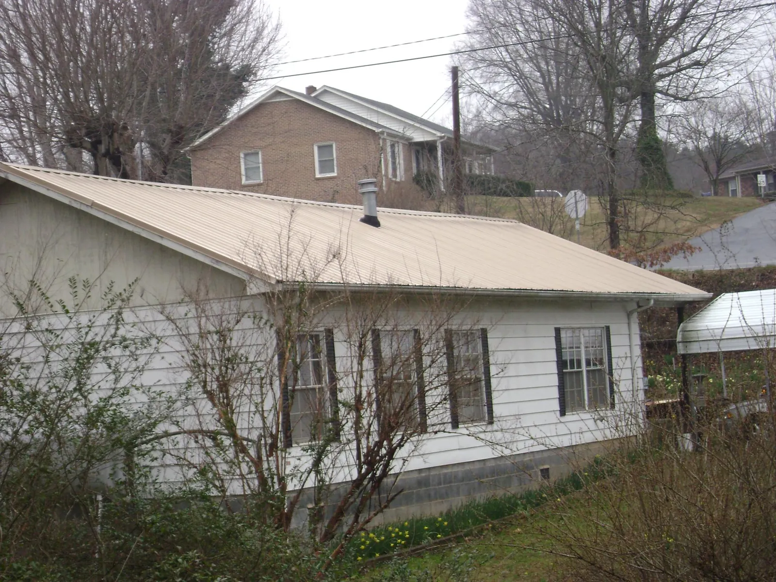 Tan metal roof on a white sided house set into a hillside — Commercial Roofing by Roofing Brothers in Stoughton